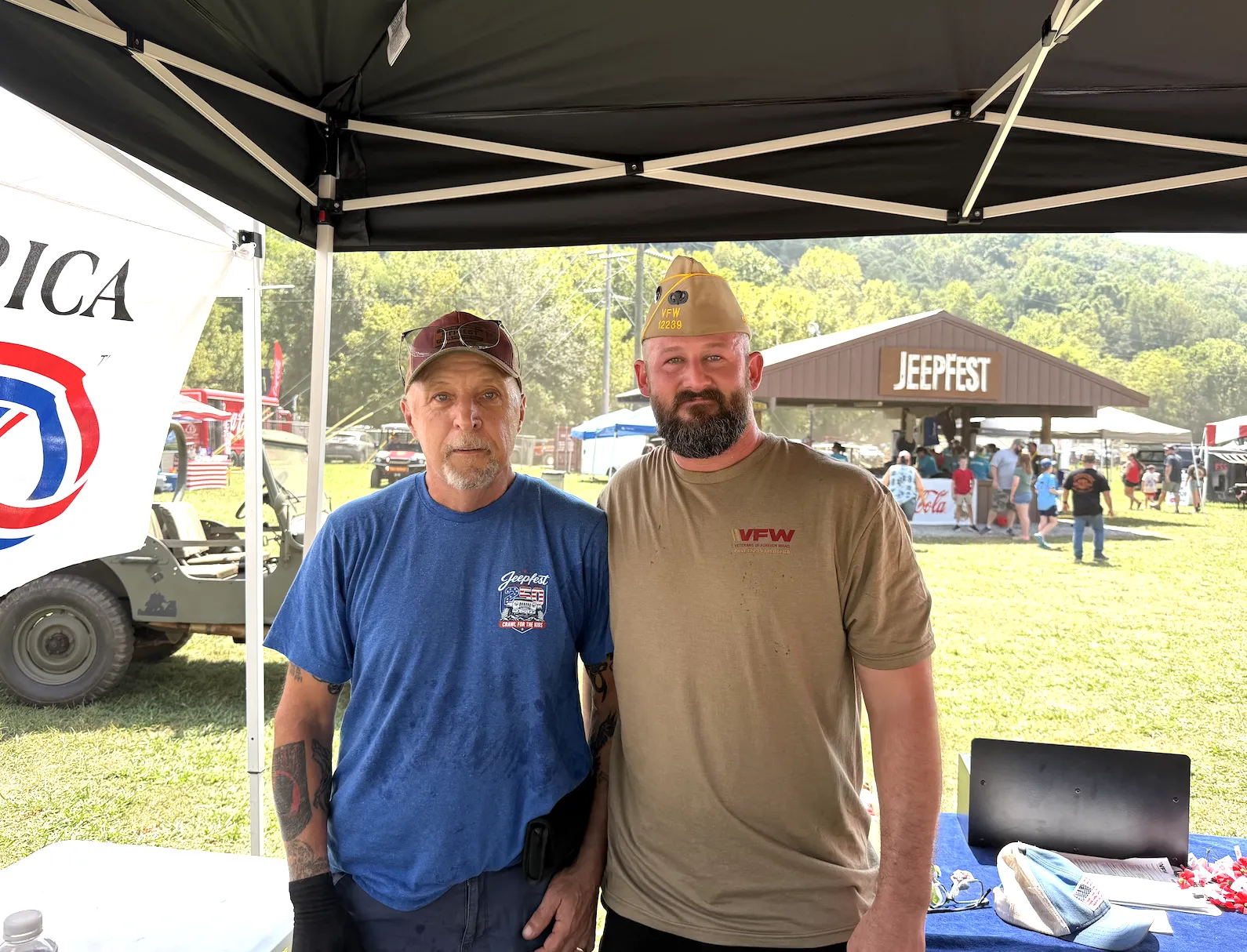 Two volunteers stand at the booth with the JeepFest sign and Buddy Poppies visible.