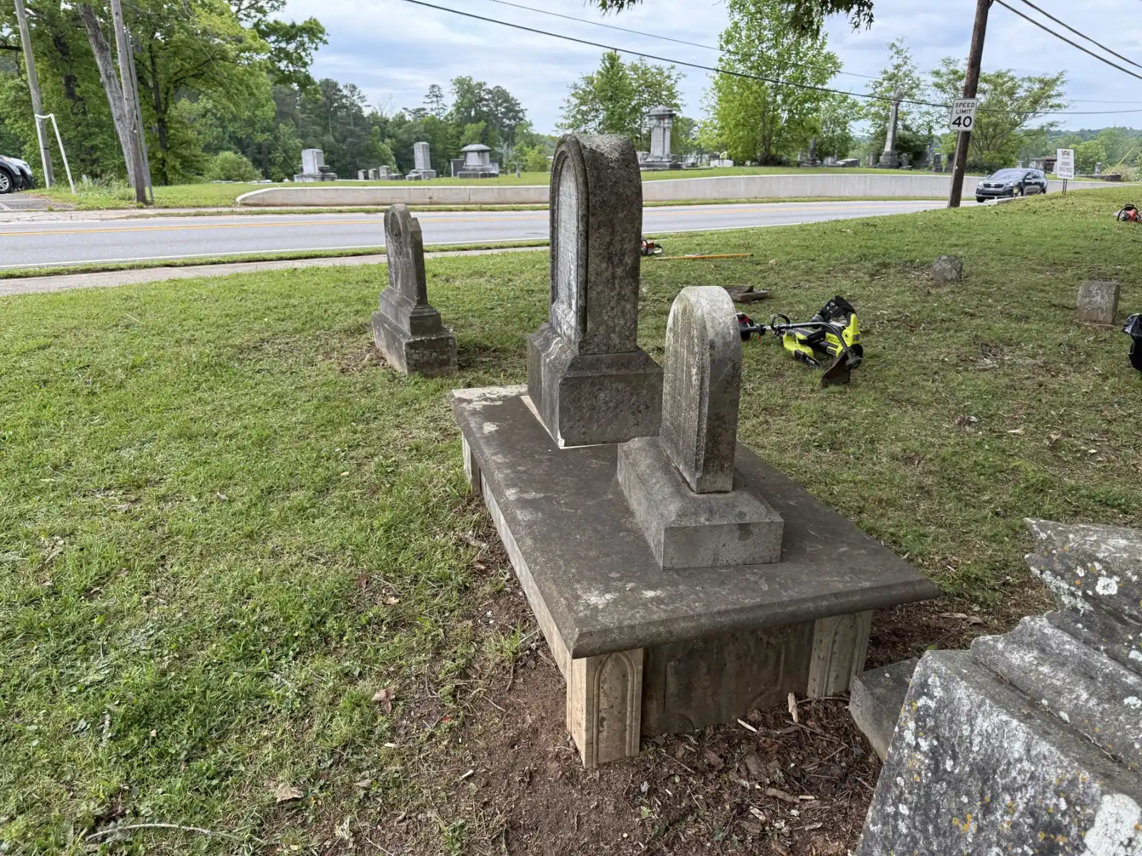 Historic family grave markers with trimmed grass and cleanup equipment nearby.