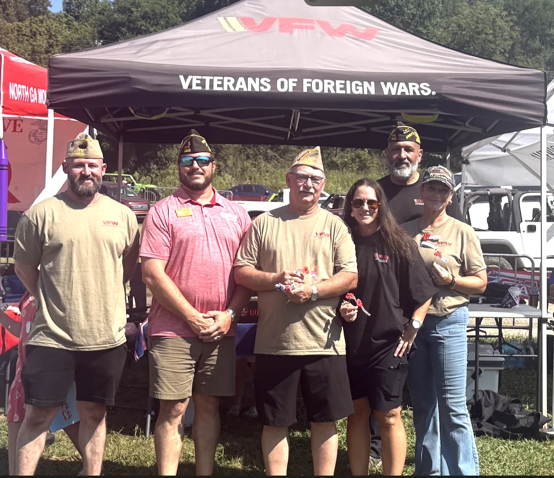 Six volunteers pose with Buddy Poppies beneath a Veterans of Foreign Wars canopy.