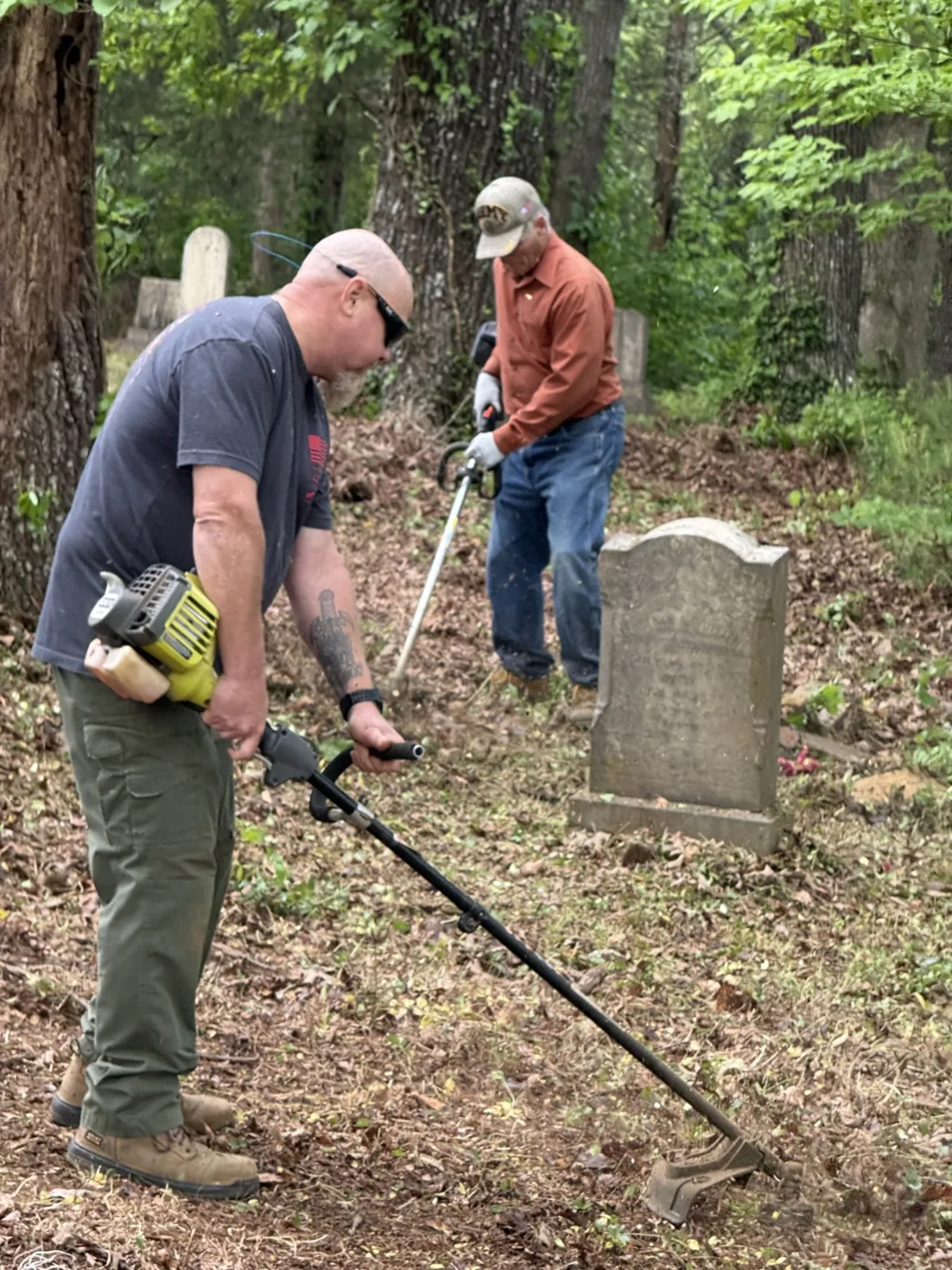 Two volunteers use string trimmers among historic gravestones.
